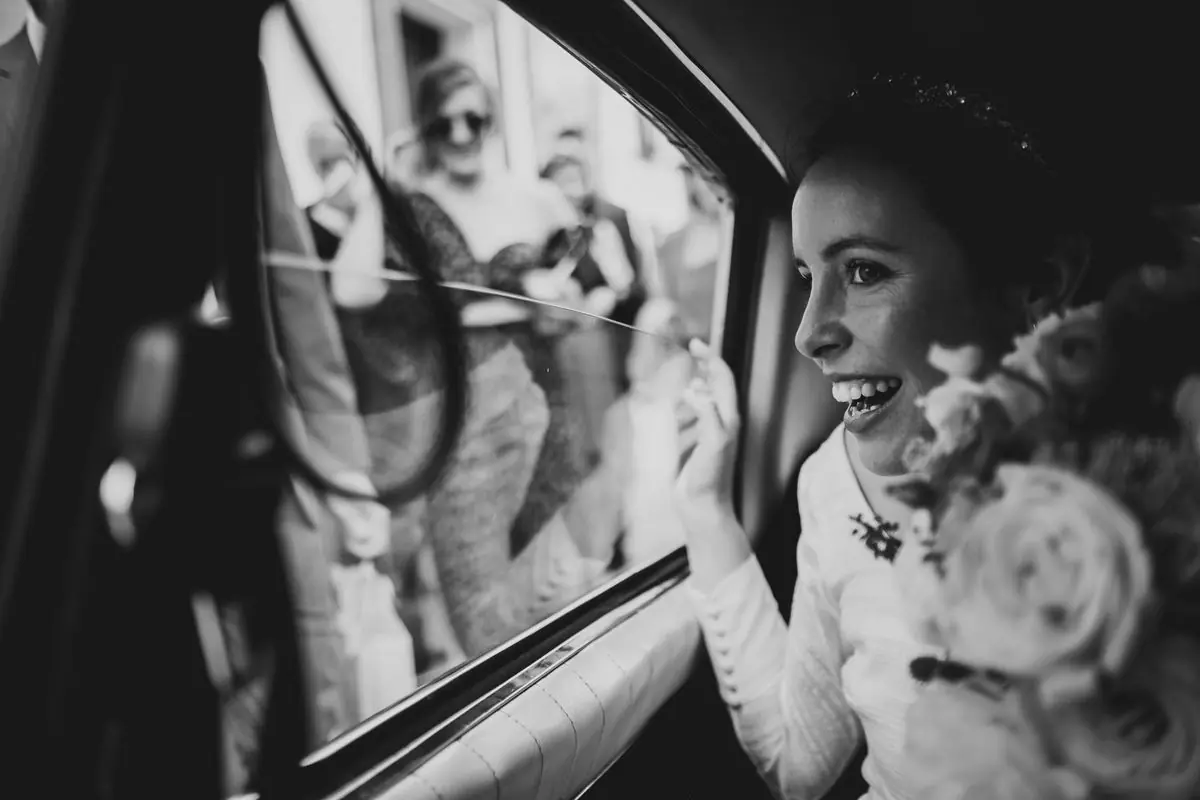 La novia riéndose asomada a la ventanilla del coche