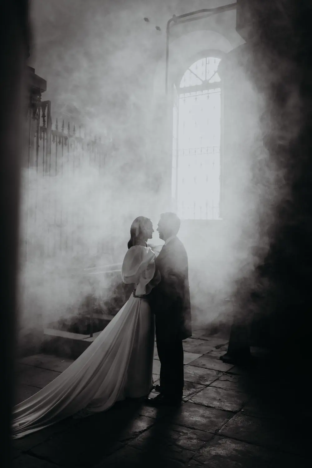 Los novios abrazados entre el humo frente a una ventana