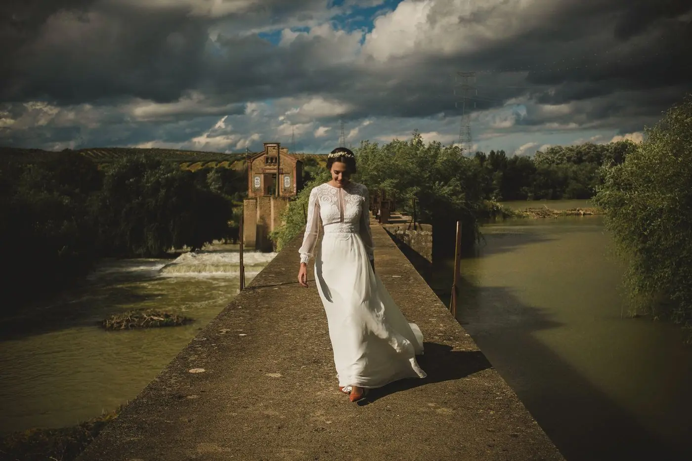 La novia caminando sola por una presa bajo un cielo de tormenta
