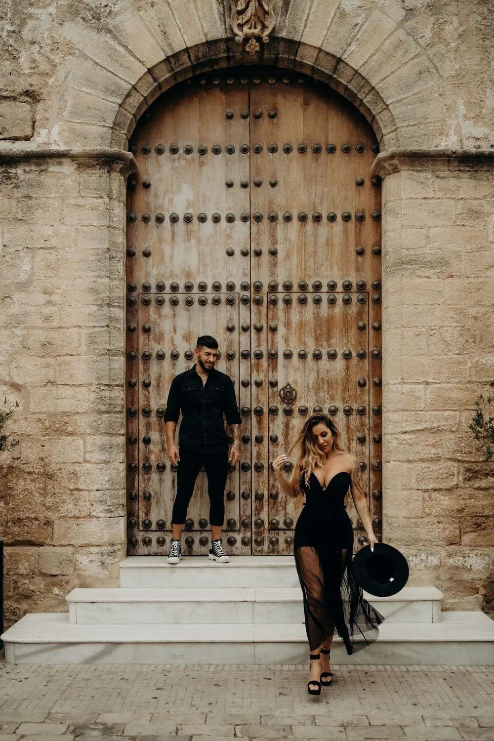 Una pareja vestida de negro frente a un gran portón de madera