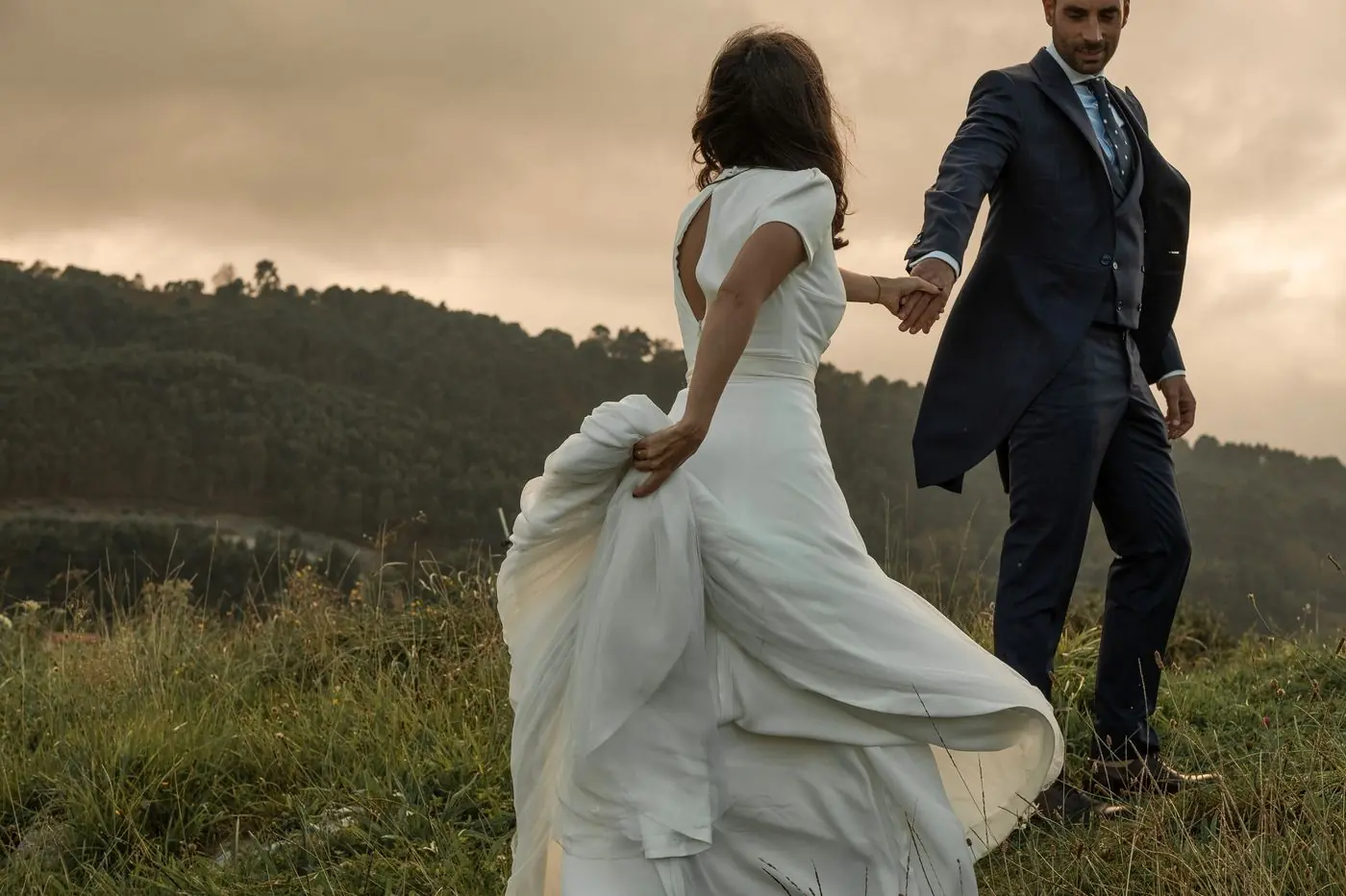 Los novios caminando de la mano por el campo al atardecer